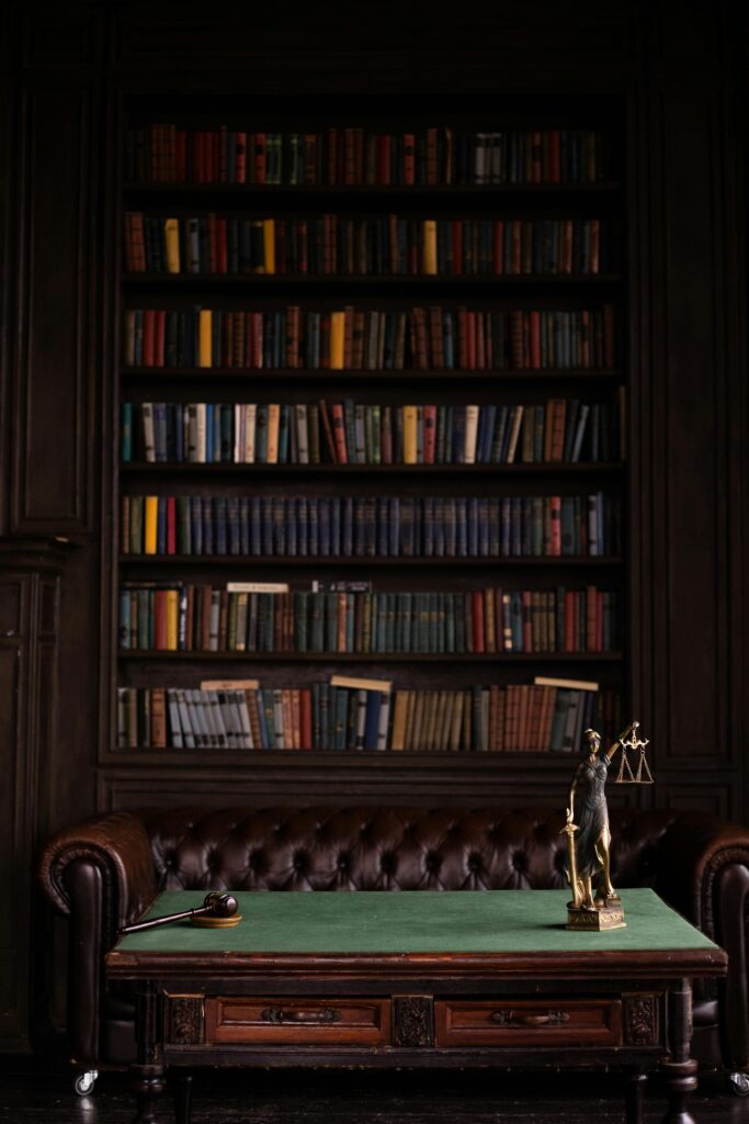 A sophisticated library scene featuring a leather sofa, bookshelves, and a statue of justice with a gavel on the table.